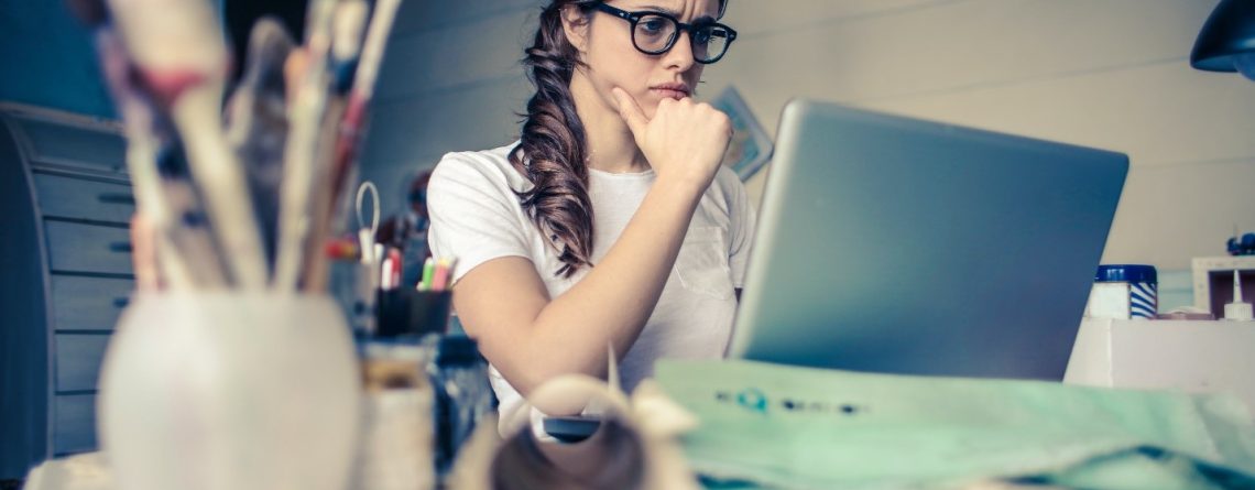 A woman in glasses is sitting at a desk with a laptop, seeking academic assistance.