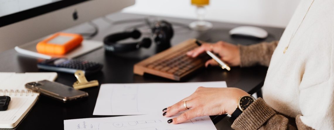 A woman working at a desk with a laptop and papers working on her essay.
