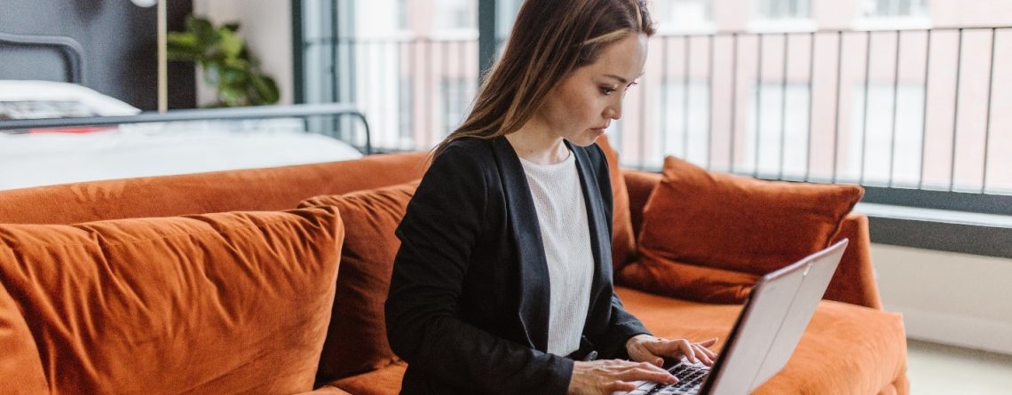 A woman, who struggles with argumentative writing, sits on a couch using a laptop.