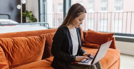 A woman, who struggles with argumentative writing, sits on a couch using a laptop.