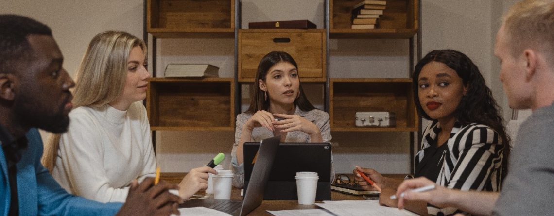 A group of people discussing the various essay writing services while sitting around a table in an office.