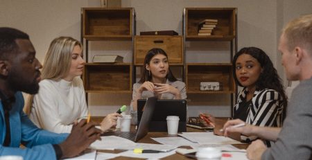 A group of people discussing the various essay writing services while sitting around a table in an office.