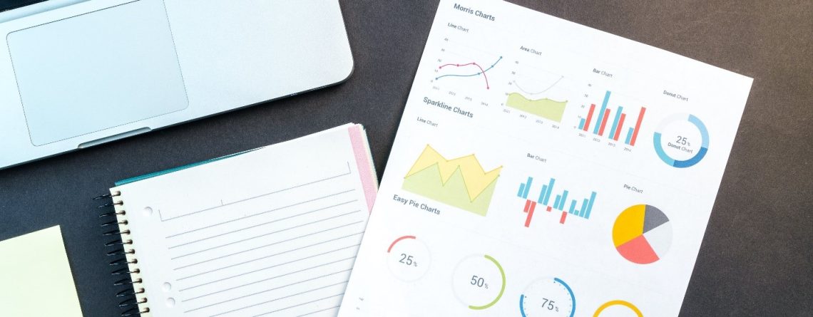 A notebook with statistical graphs on it and a laptop next to it.