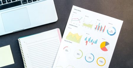 A notebook with statistical graphs on it and a laptop next to it.