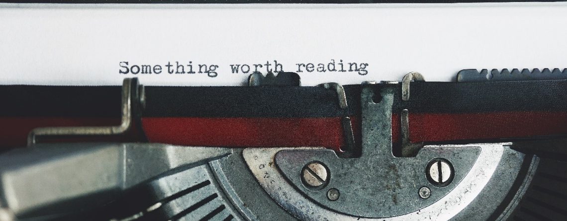 Vintage typewriter with a sheet of paper emerging, displaying the text "something worth reading." This image symbolizes the blog's purpose to guide readers in crafting effective essay outlines.
