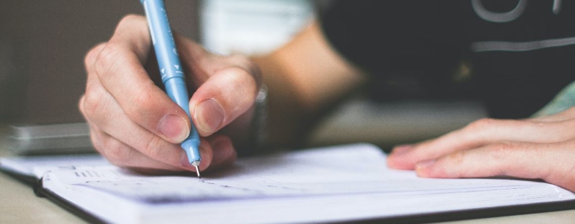 A young student writing essay in his notebook with a pen.