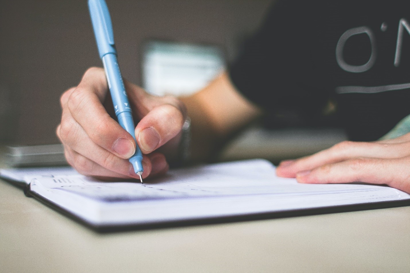 A young student writing essay in his notebook with a pen.