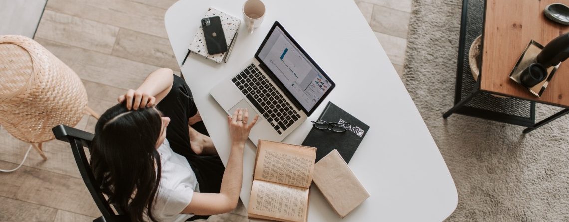 A woman at a desk with a laptop and books is looking for an inspiration for her essay.
