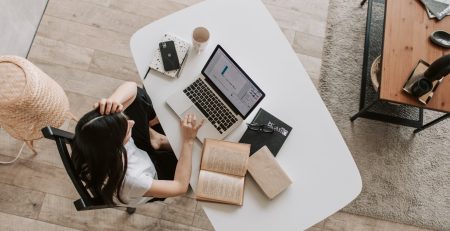 A woman at a desk with a laptop and books is looking for an inspiration for her essay.