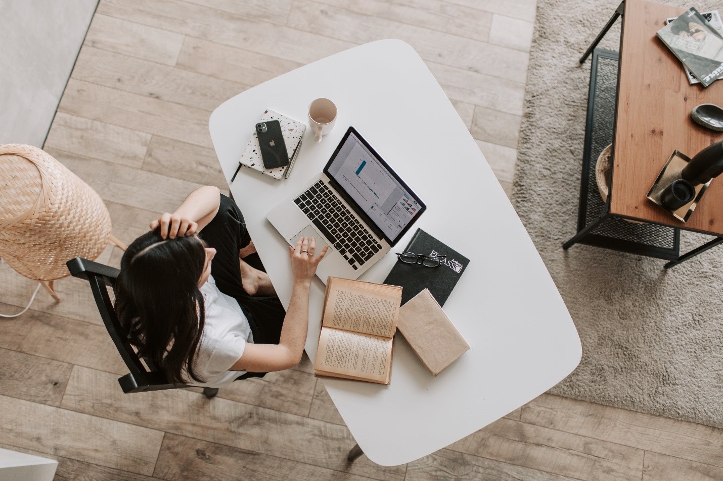 A woman at a desk with a laptop and books is looking for an inspiration for her essay.